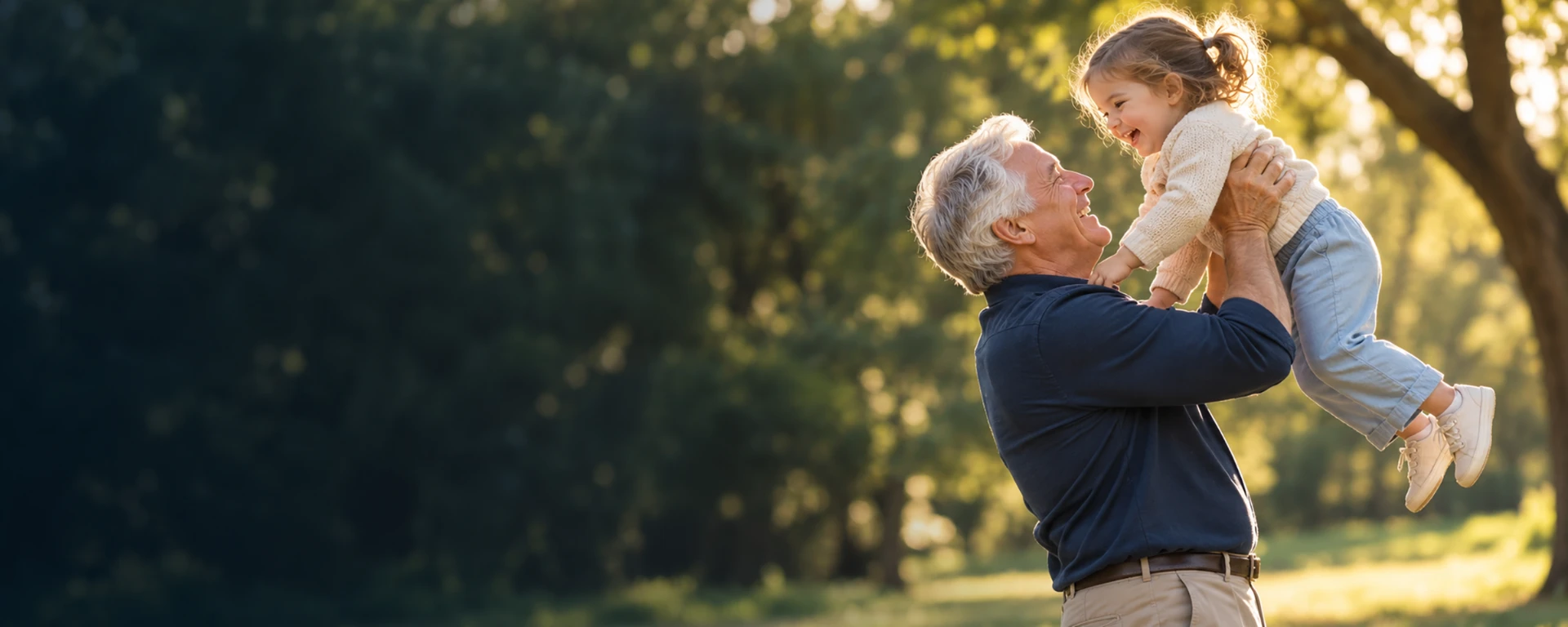 Grandfather lifting his laughing granddaughter in a sunlit park
